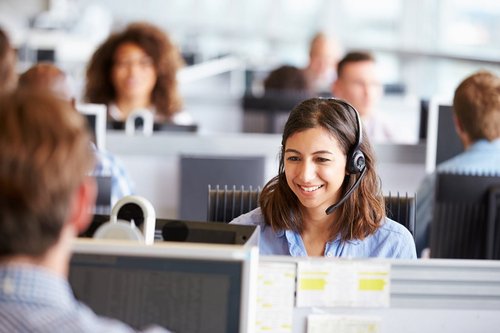 Call center agent wearing a headset, smiling at her workstation